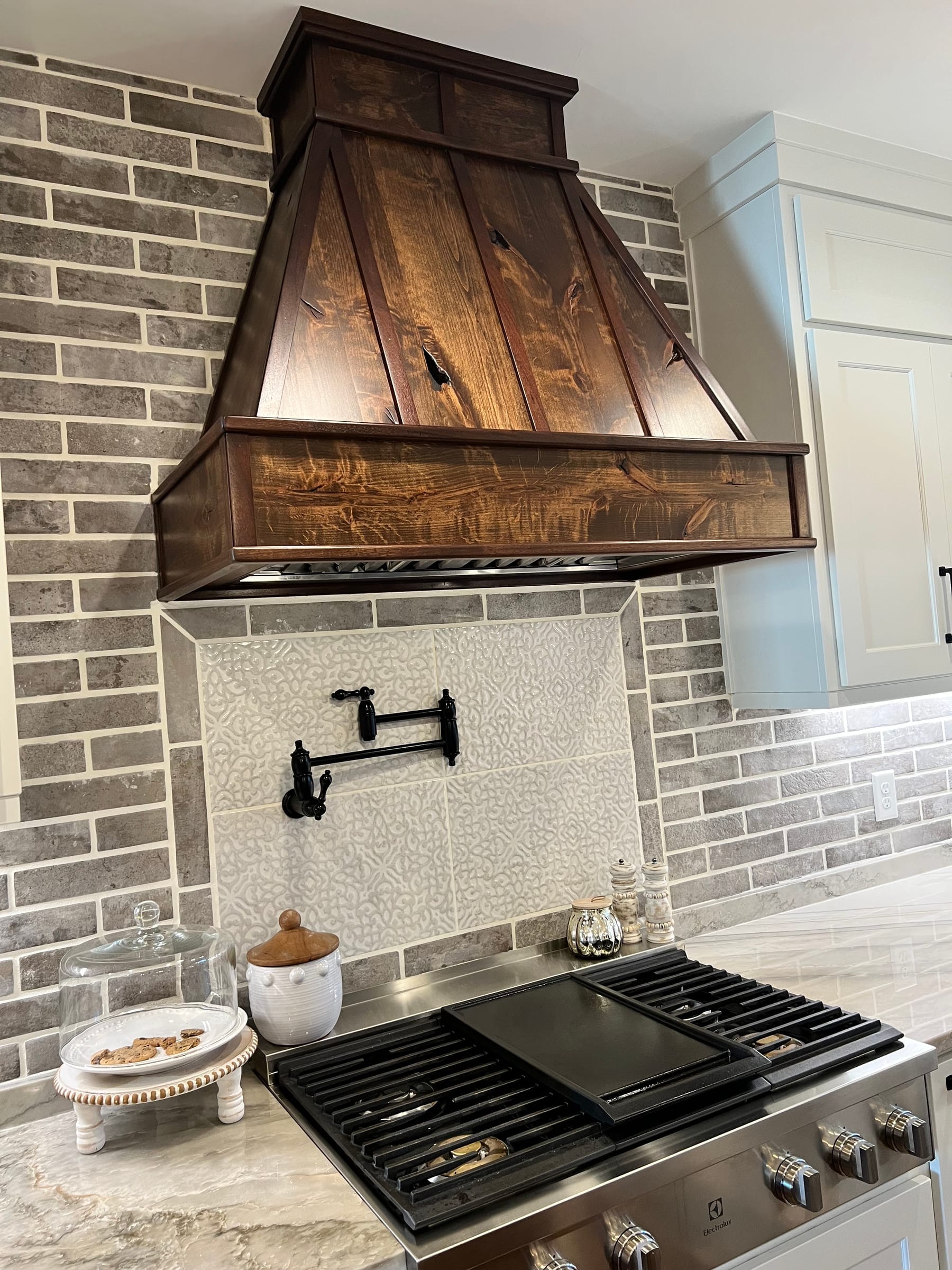 Stained plank range hood over a brick backsplash